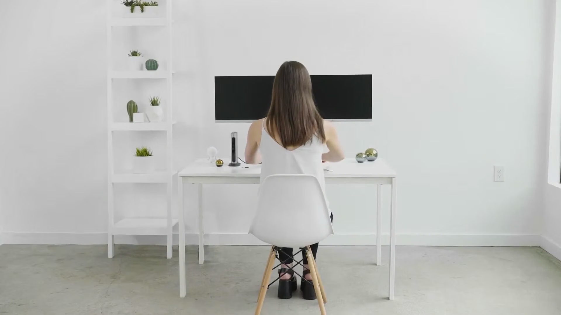 A carefully styled white workspace with a woman seated at dual monitors, from Paul’s Plugable commercial.